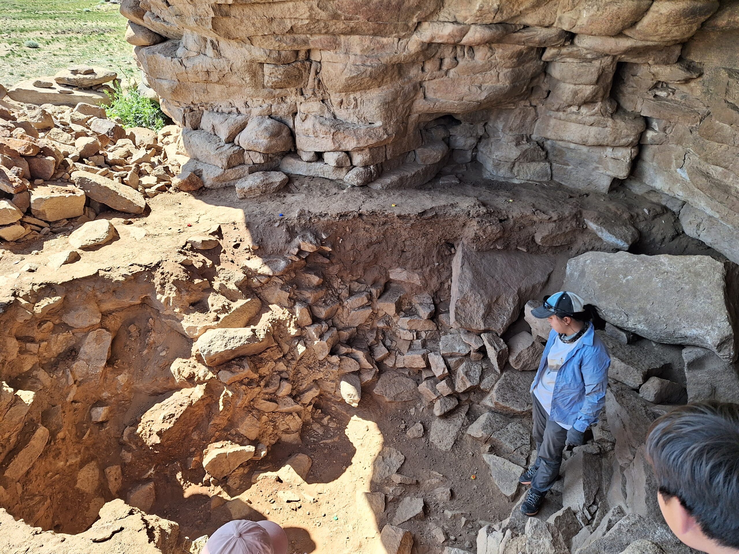 A person standing at the bottom of an excavated archaeological site surrounded by stones and artefacts.