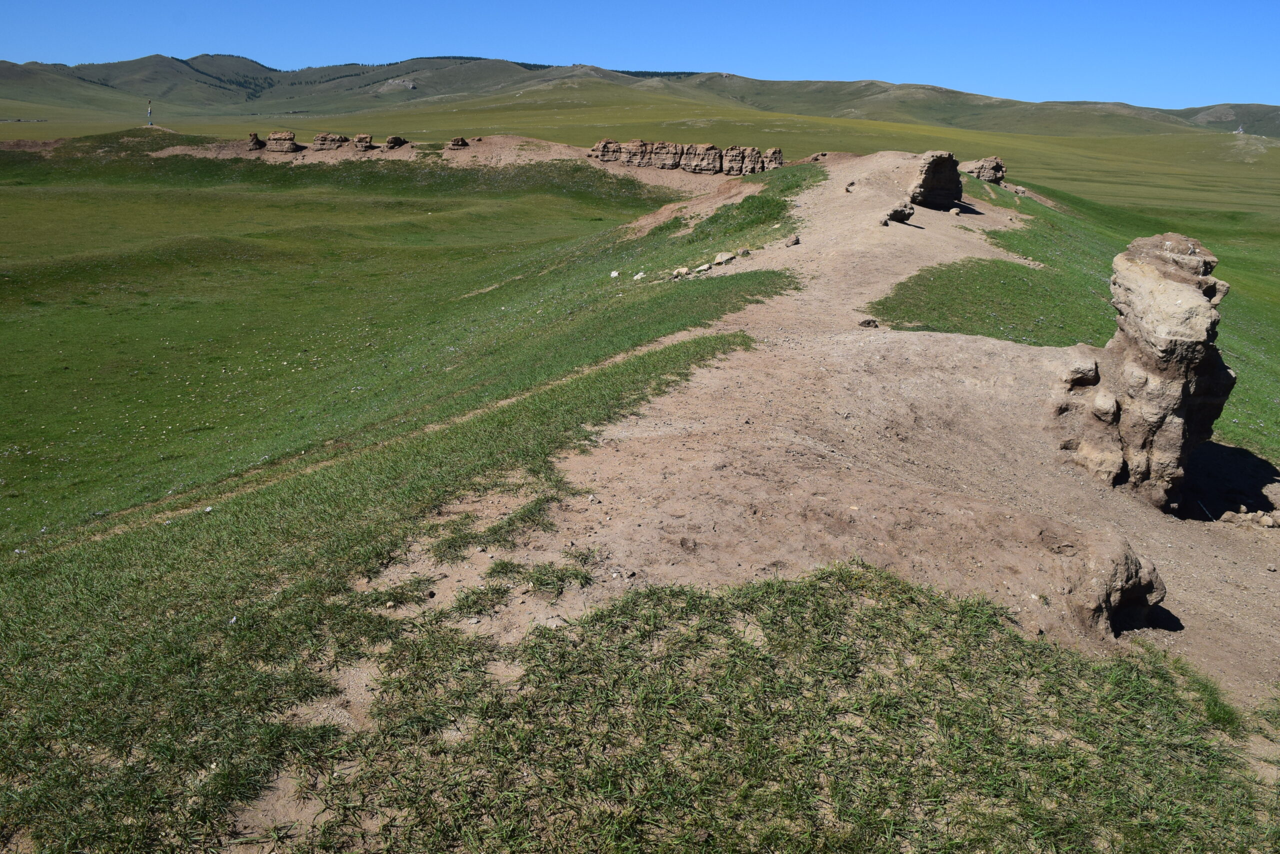 A photo of the archaeological ruins of an ancient city in Mongolia, covered in grass on an open field.