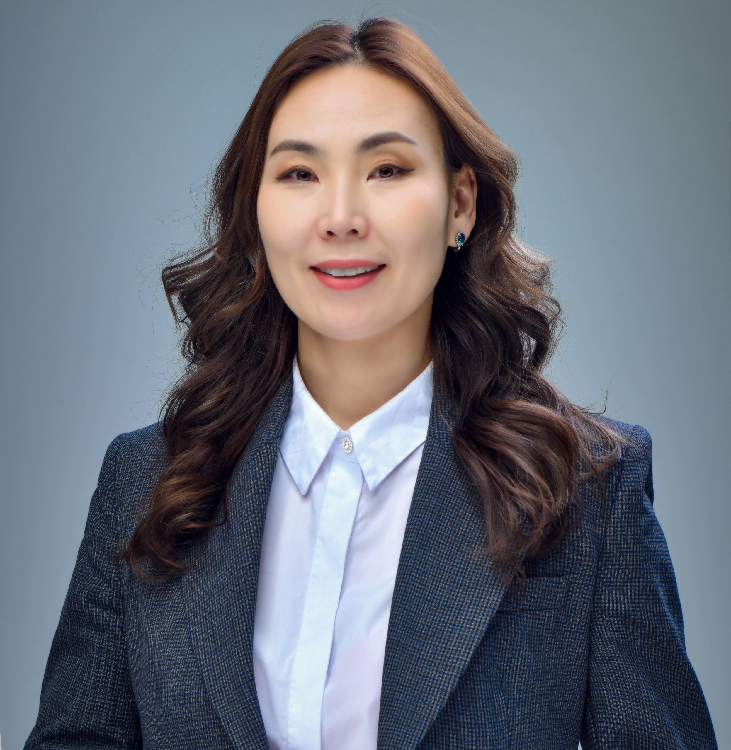 A Mongolian woman with long, dark hair wearing a charcoal gray blazer and a white button-down shirt smiles into the camera