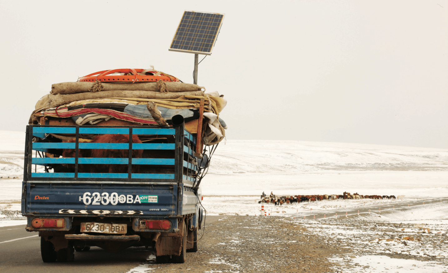 A photo of a truck hauling a nomadic family's ger and personal belongings down a snowy dirt road in the Mongolian countryside.