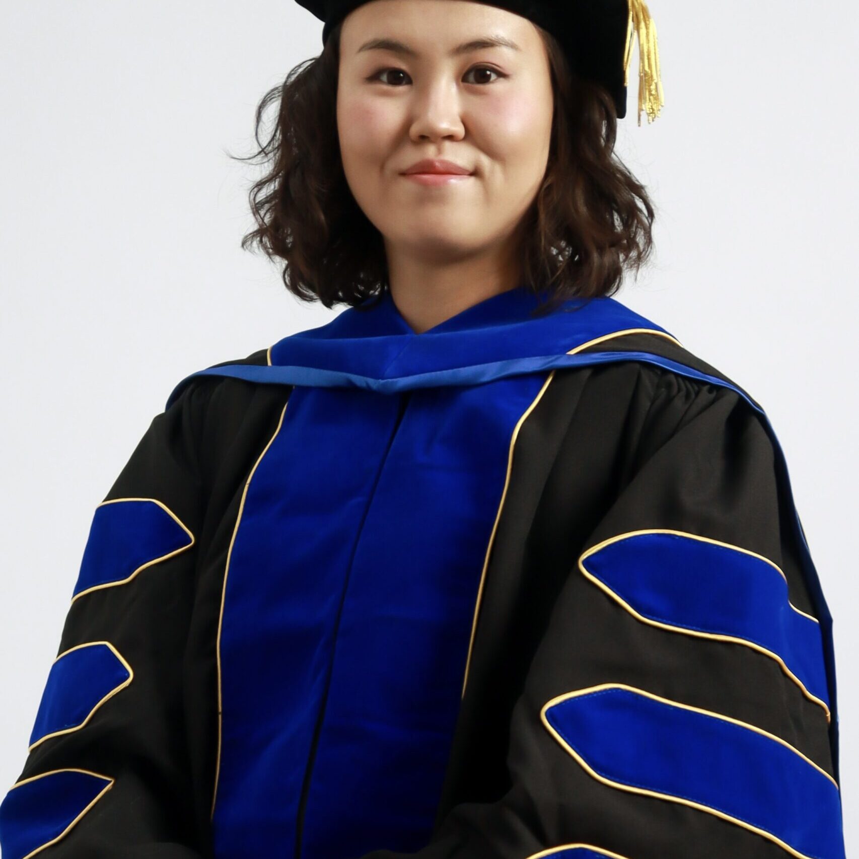 A photo of a young Mongolian woman wearing doctoral robes looking directly at the camera.