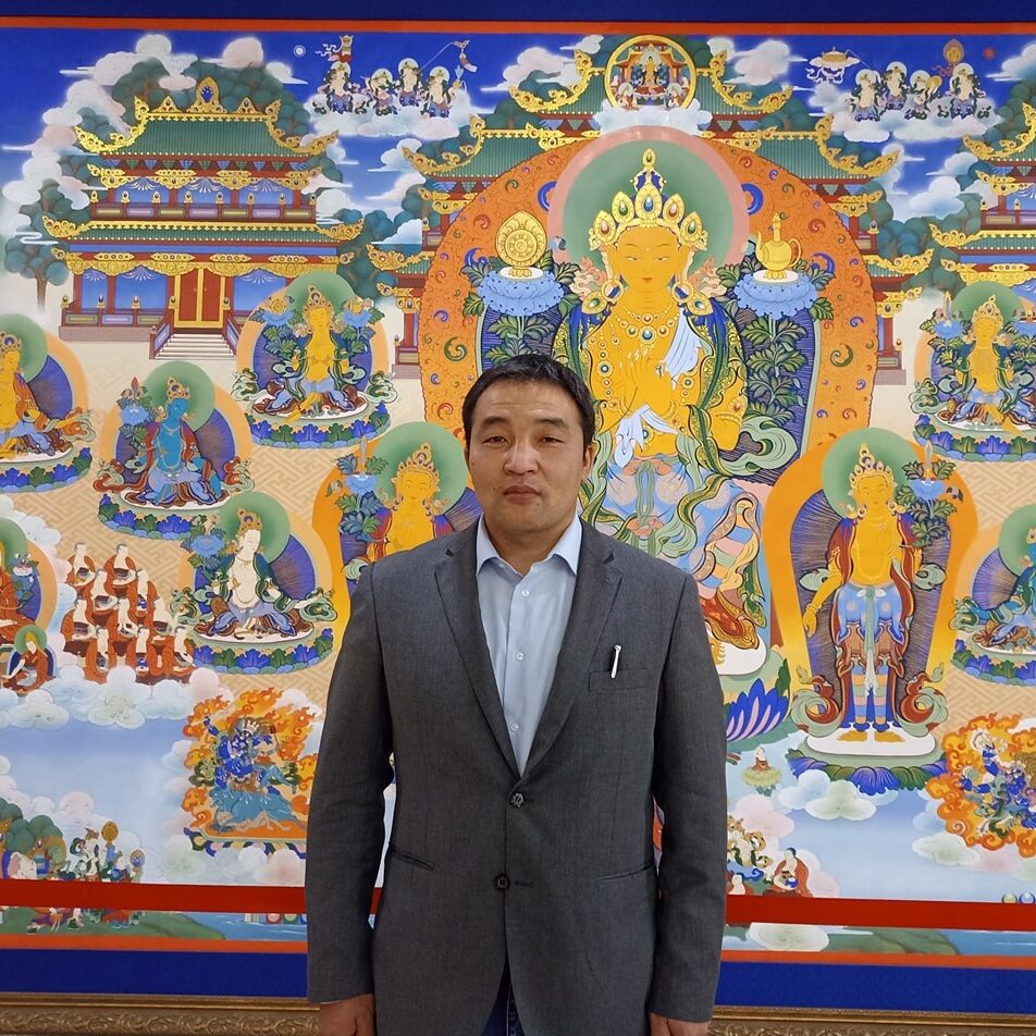 A photo of a man in a suit standing in front of a Buddhist painting.