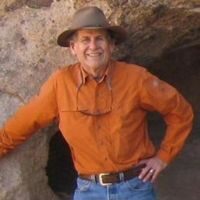 A picture of a man in a hat and an orange shirt smiling at the camera.