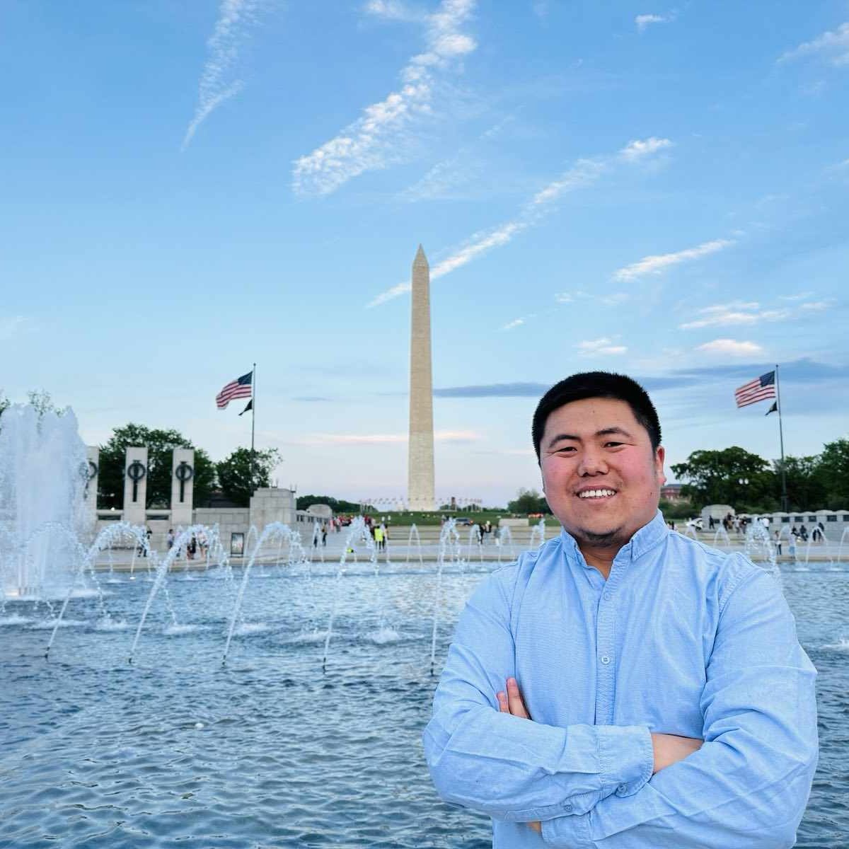 A photo of a young Mongolian man smiling and standing in front of a fountain.